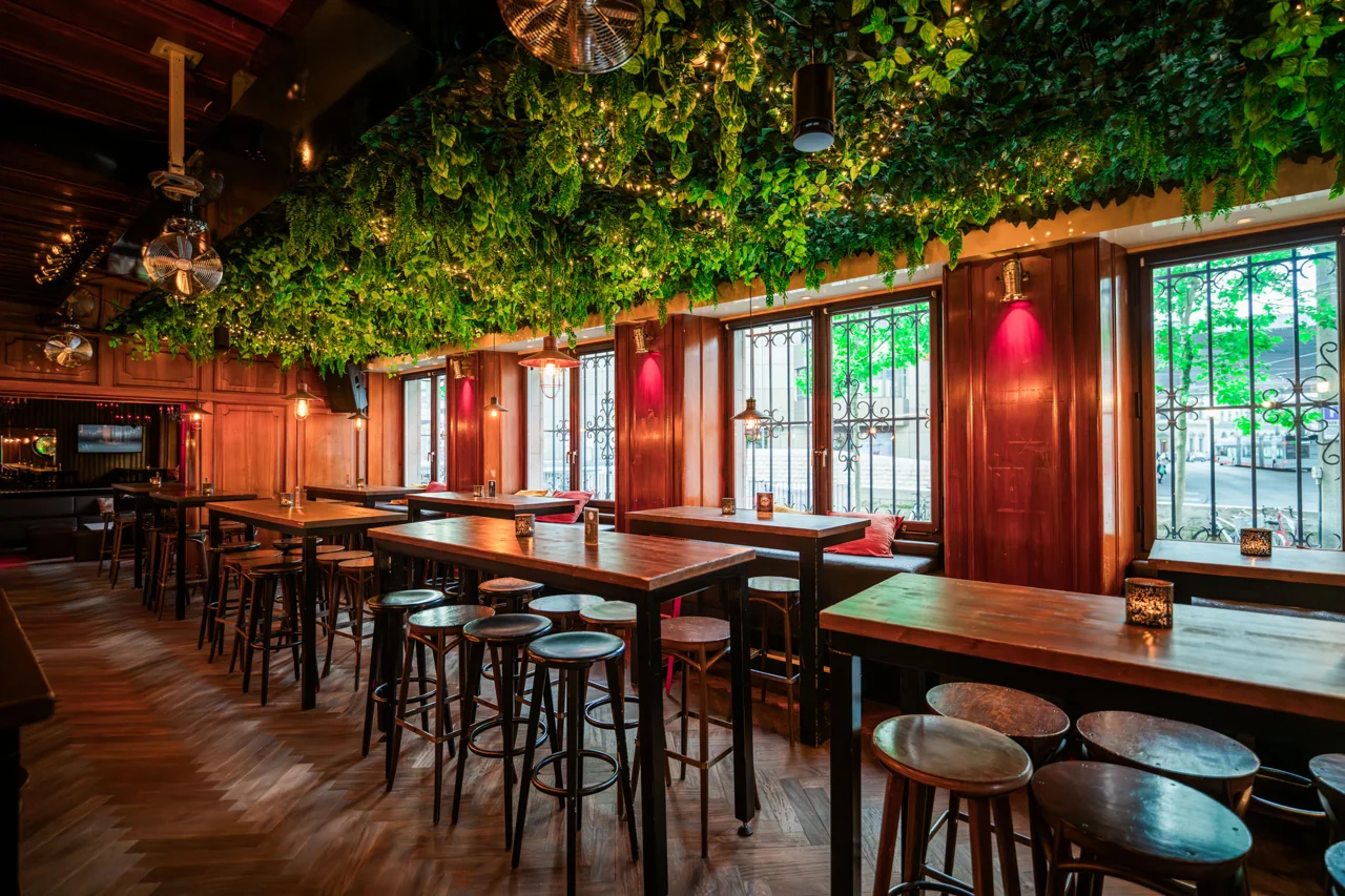 Hohe Holztische entlang der Fensterfront in der Arch-Bar