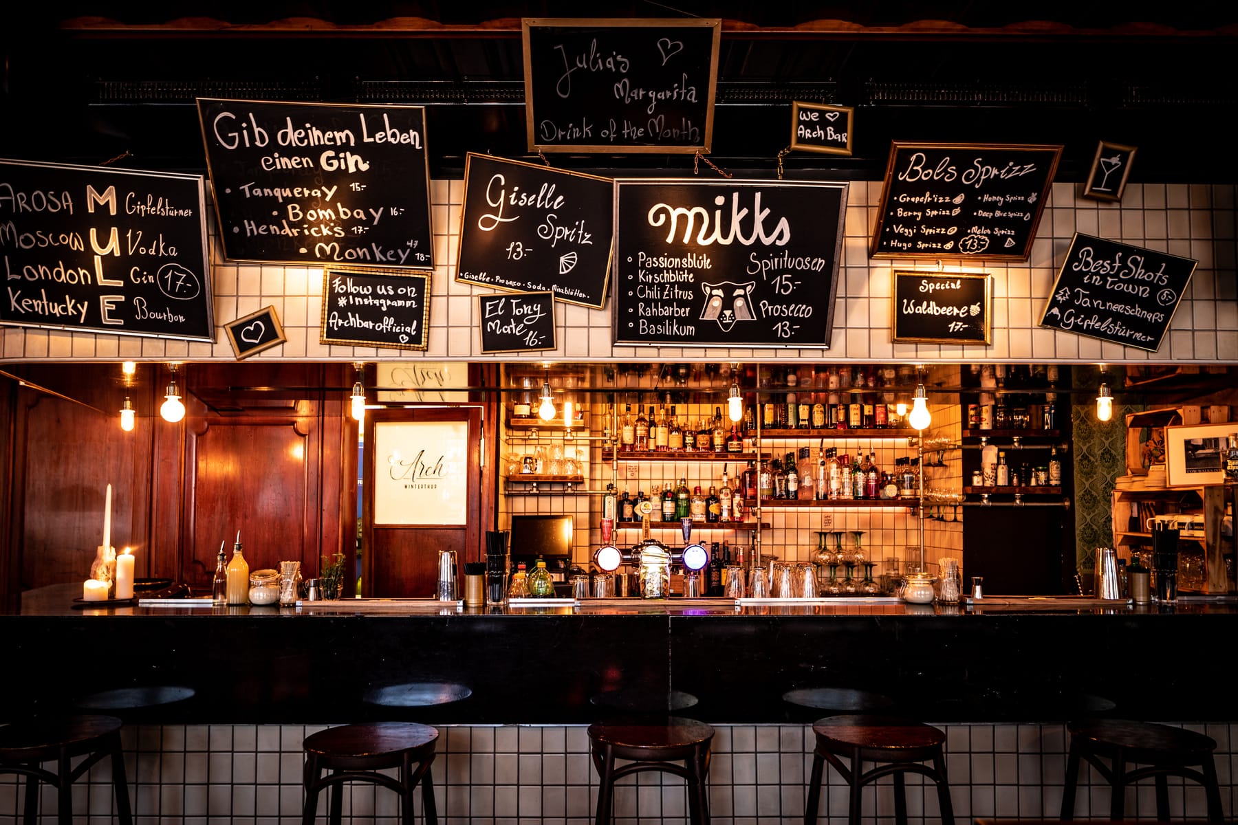 Die warm beleuchtete Arch-Bar mit Holztheke und Flaschenregalen